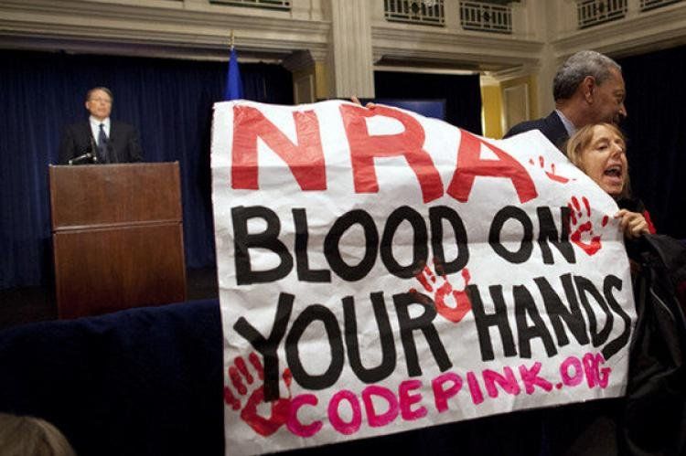 El cartel denuncia a la NRA porque tiene sangre en las manos. Detrás, Wayne LaPierre y sus tonterías peligrosas.