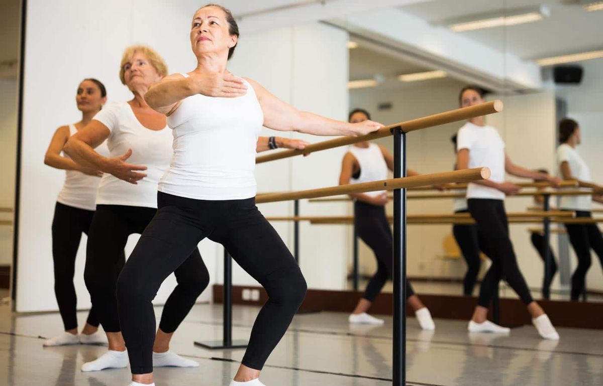 Un grupo de mujeres mayores a 50 años practican en barre en una barra de ballet.