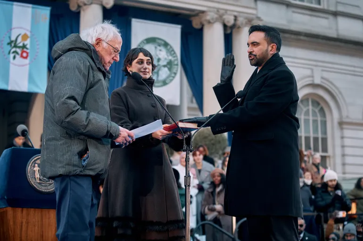 El senador estadounidense Bernie Sanders (izquierda) toma juramento al alcalde Zohran Mamdani (derecha) mientras su esposa, Rama Duwaji (centro), sostiene el Cor&aacute;n durante la ceremonia de investidura p&uacute;blica de Mamdani, el jueves 1 de enero de 2026 en Nueva York. [Andres Kudacki/AP Photo]
