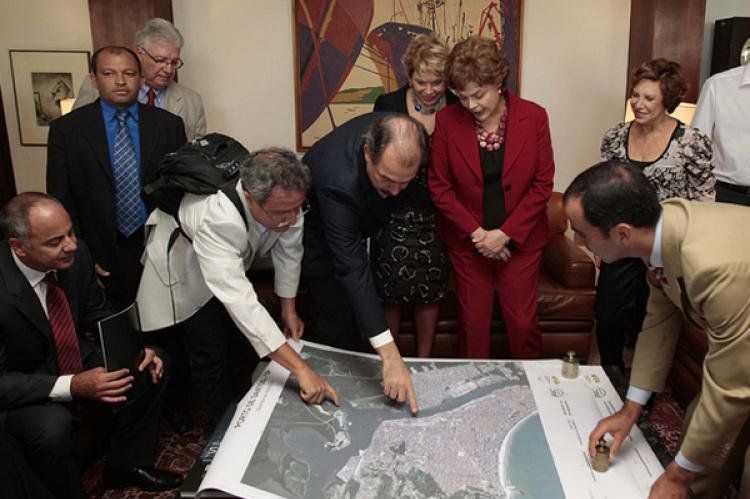 Dilma Rousseff (de rojo) y a su lado Aloizio Mercadante (de traje) mostrándole una ubicación en un mapa.