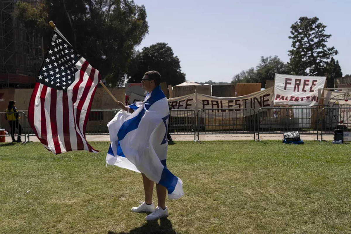 Cubierto con una bandera israelí, un partidario pro-Israel camina con una bandera estadounidense cerca del campamento pro-palestino en el campus de UCLA en Los Ángeles. Cubierto con una bandera israelí, un partidario pro-Israel camina con una bandera estadounidense cerca del campamento pro-palestino en el campus de UCLA en Los Ángeles.