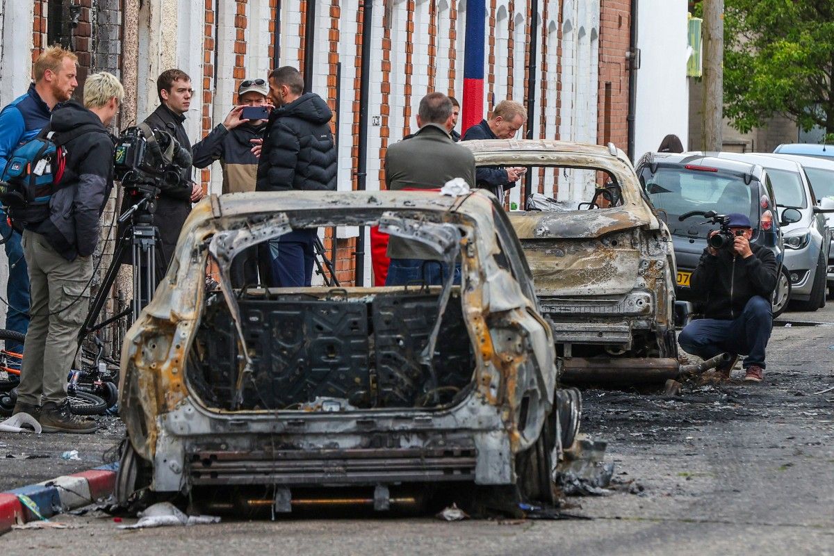 Varios vecinos observan los daños en Belfast tras una noche de violencia racista que dejó casas, autos y familias migrantes bajo ataque. Varios vecinos observan los daños en Belfast tras una noche de violencia racista que dejó casas, autos y familias migrantes bajo ataque.