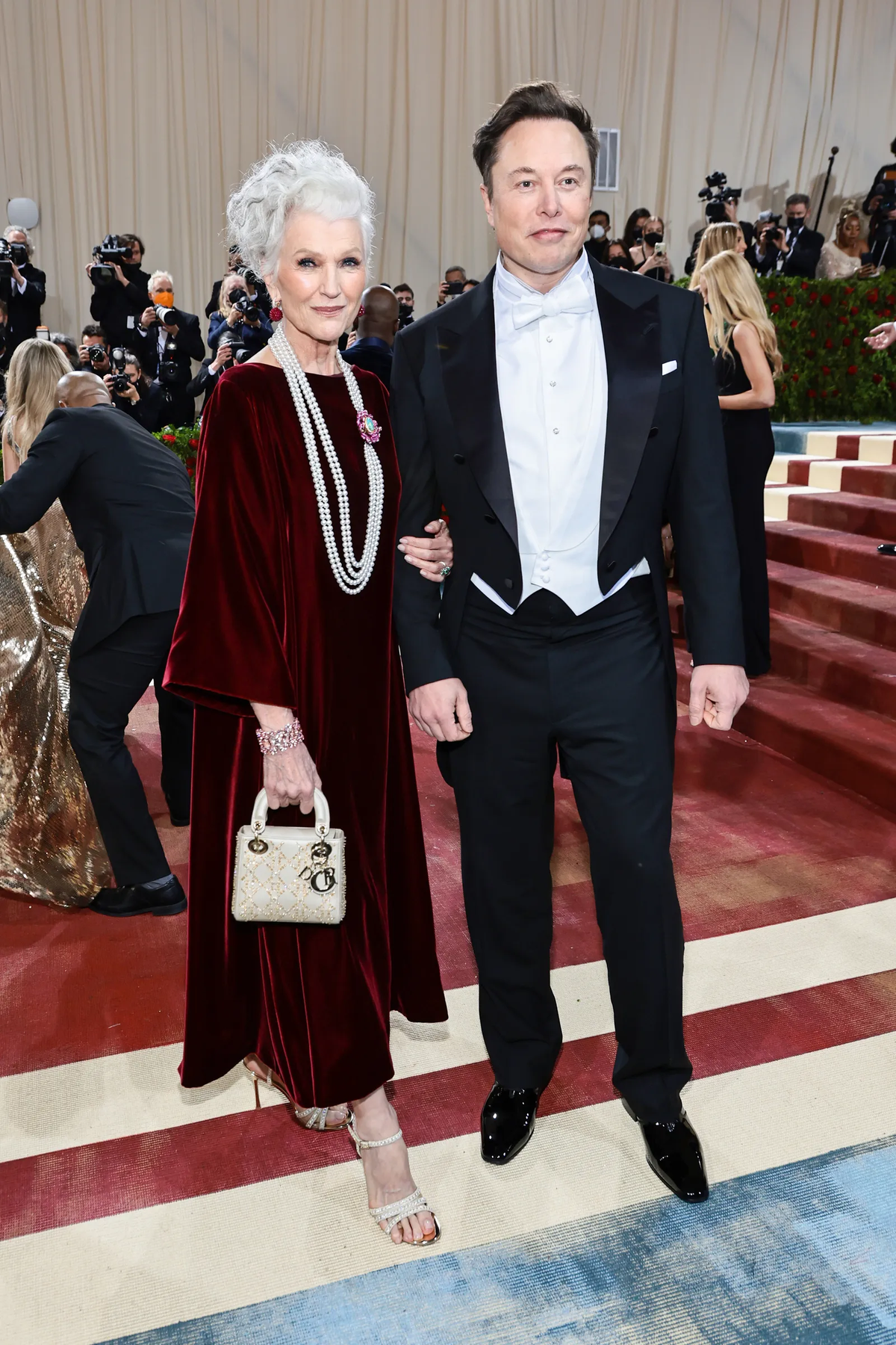 Maye Musk ha aparecido con un vestido carmesí de terciopelo de Dior, con cuatro vueltas de perlas colgando del cuello sujetas al pecho por un broche de Chopard. Por su parte, Elon se limitó a respetar el dress code con un esmoquin vintage.
