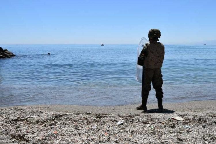 Soldado español de guardia en Ceuta, mientras un migrante nada hacia la costa.